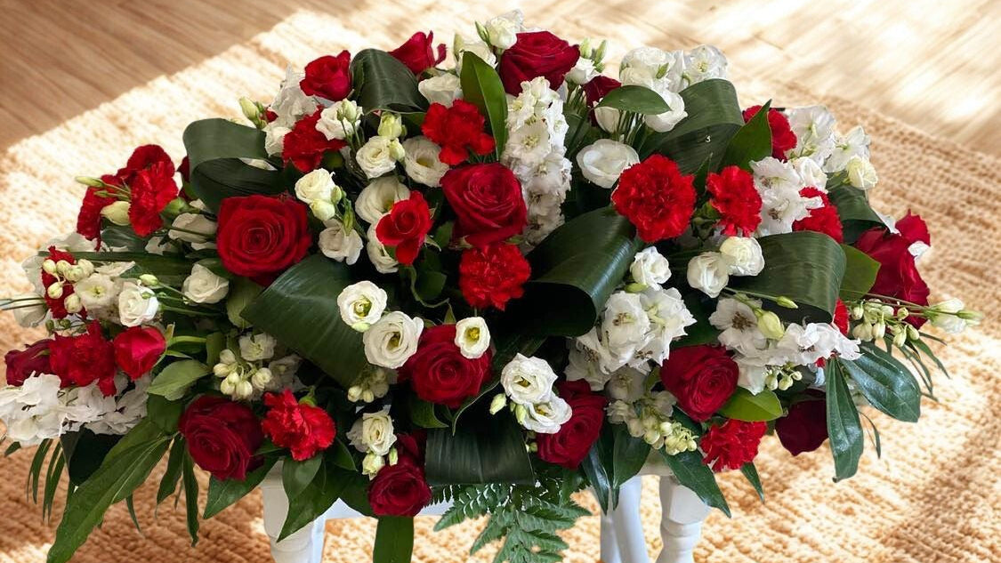 Coffin spray of red, white, and green flowers on a wooden surface